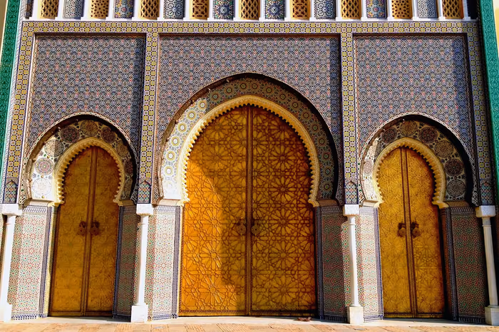 Ornate brass doors framed by zellige tilework at a Moroccan royal palace