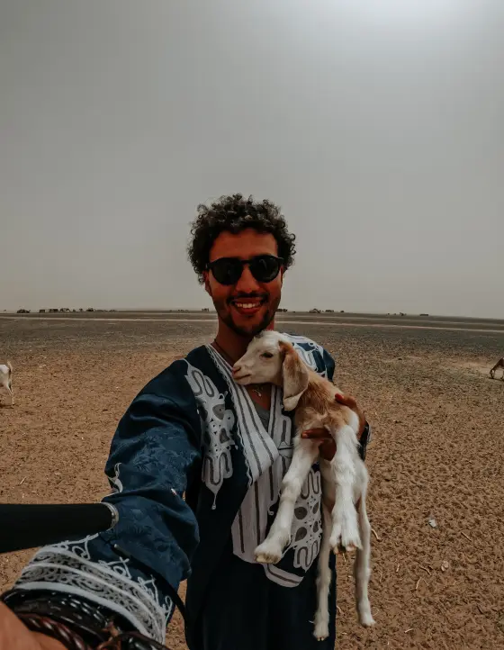 Mohamed Abira holding a young goat on the hard desert plain near Merzouga