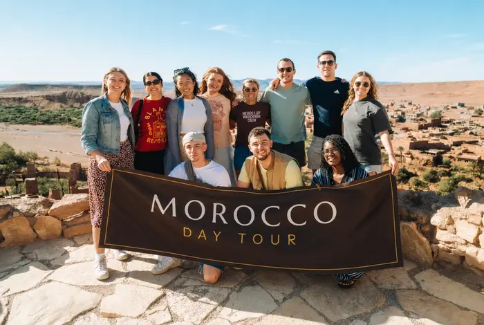 A Morocco Day Tour group holding the company banner above the kasbah at Ait Ben Haddou